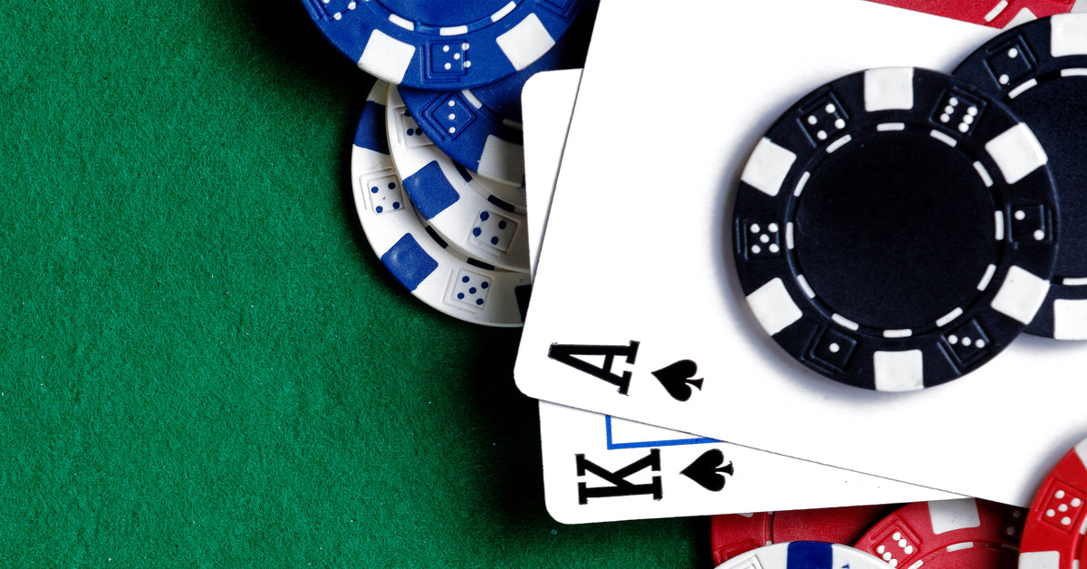 An overhead view of playing cards and gambling chips on a green table felt with the king and ace of spades showing.