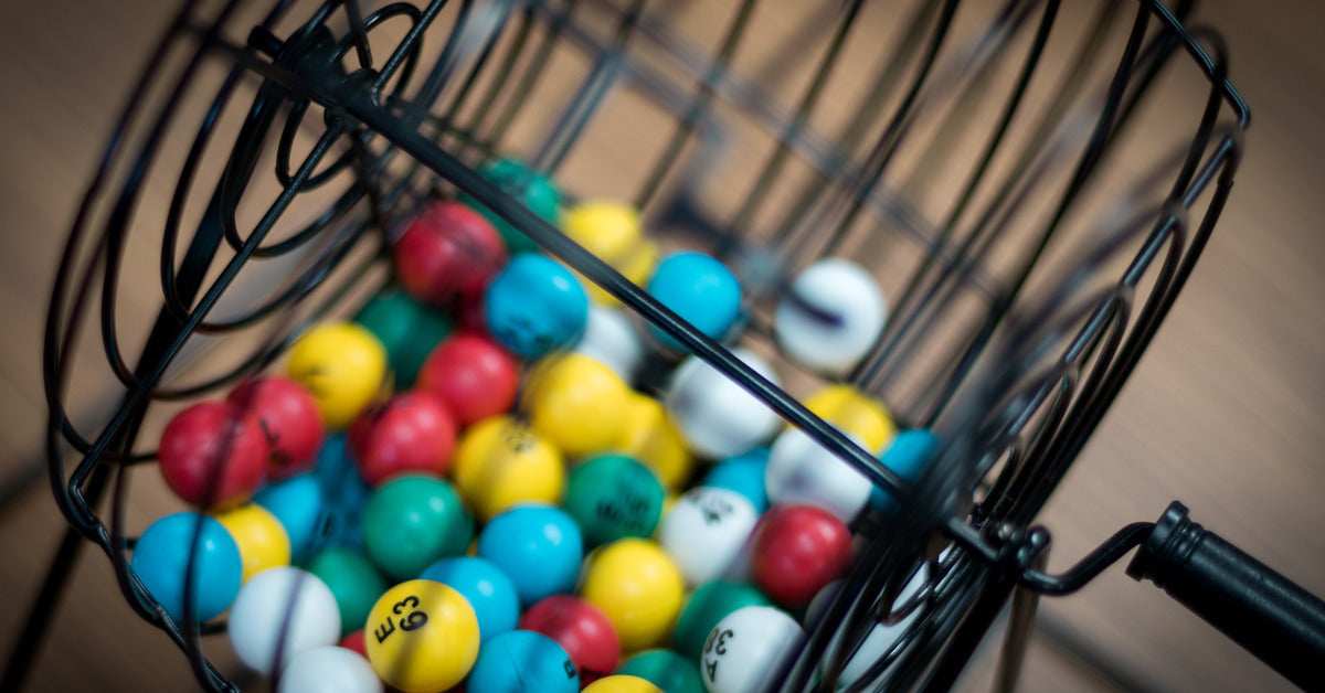 A close-up of a black rolling bingo ball cage with various colored and numbered small bingo balls inside.