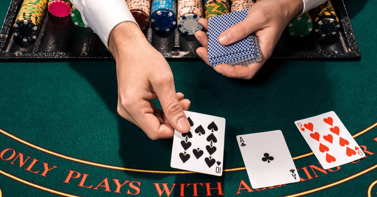 A close-up of a casino dealer's hands laying down three cards face-up over a green blackjack table layout with chips.