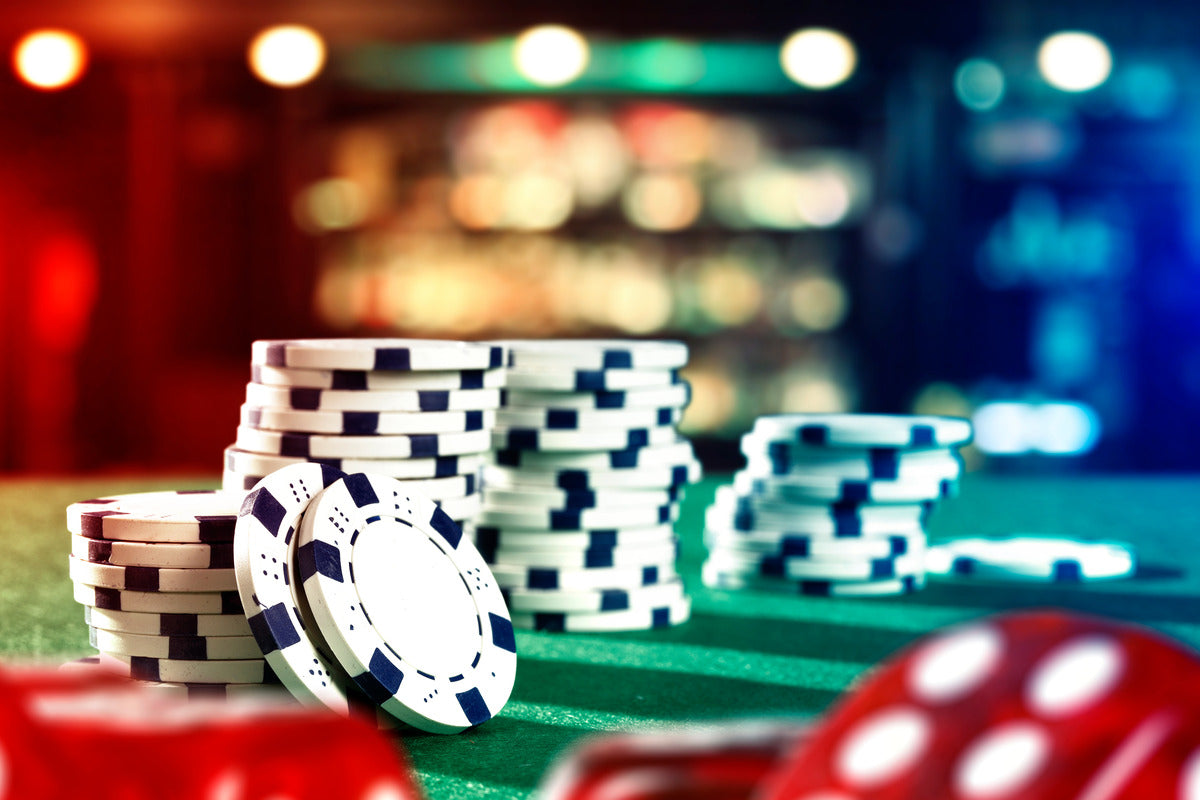 Multiple stacks of black and white poker chips lined up on a green felt surface with red dice in the foreground.