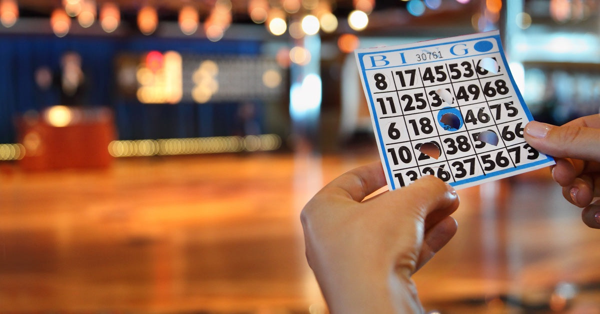  A person holding a blue bingo card with the glare of blurred string lights in the distance in front of them.