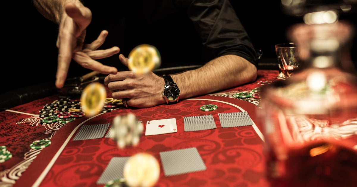 A person throws poker chips on the red surface of a poker table as cards lay in front of them.