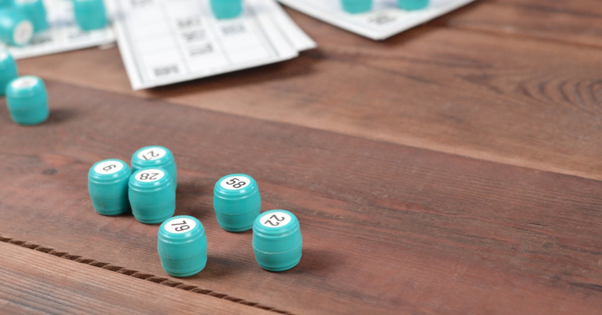 A table with bingo cards and numerous miniature blue barrels on it. Each barrel has a white sticker with a number on top.